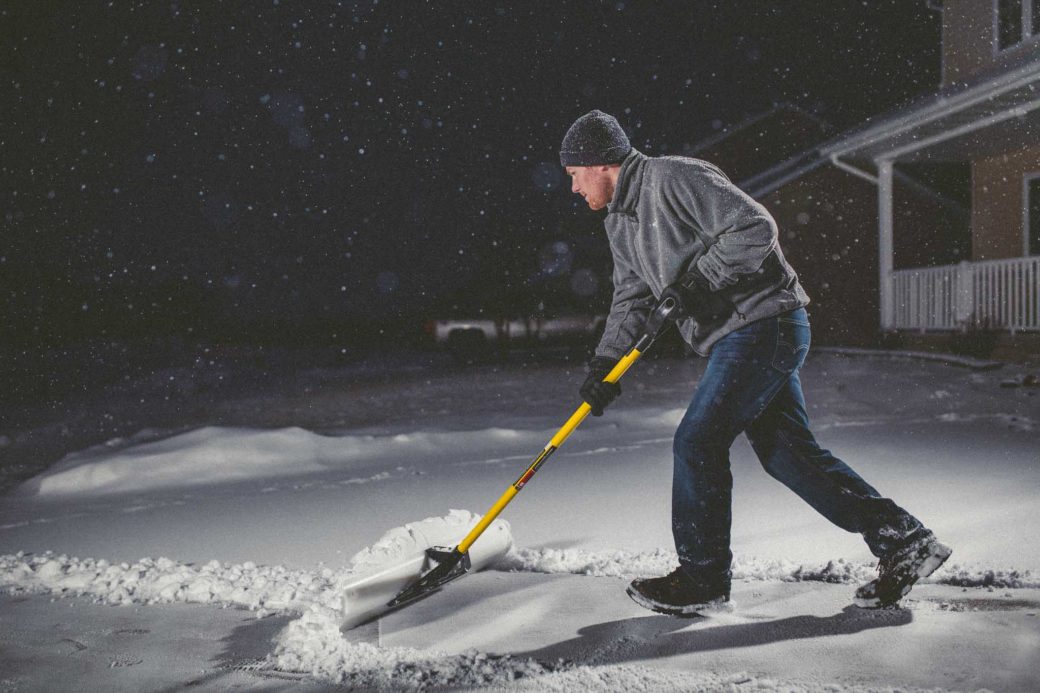 Lifestyle photo of many pushing snow with shovel.