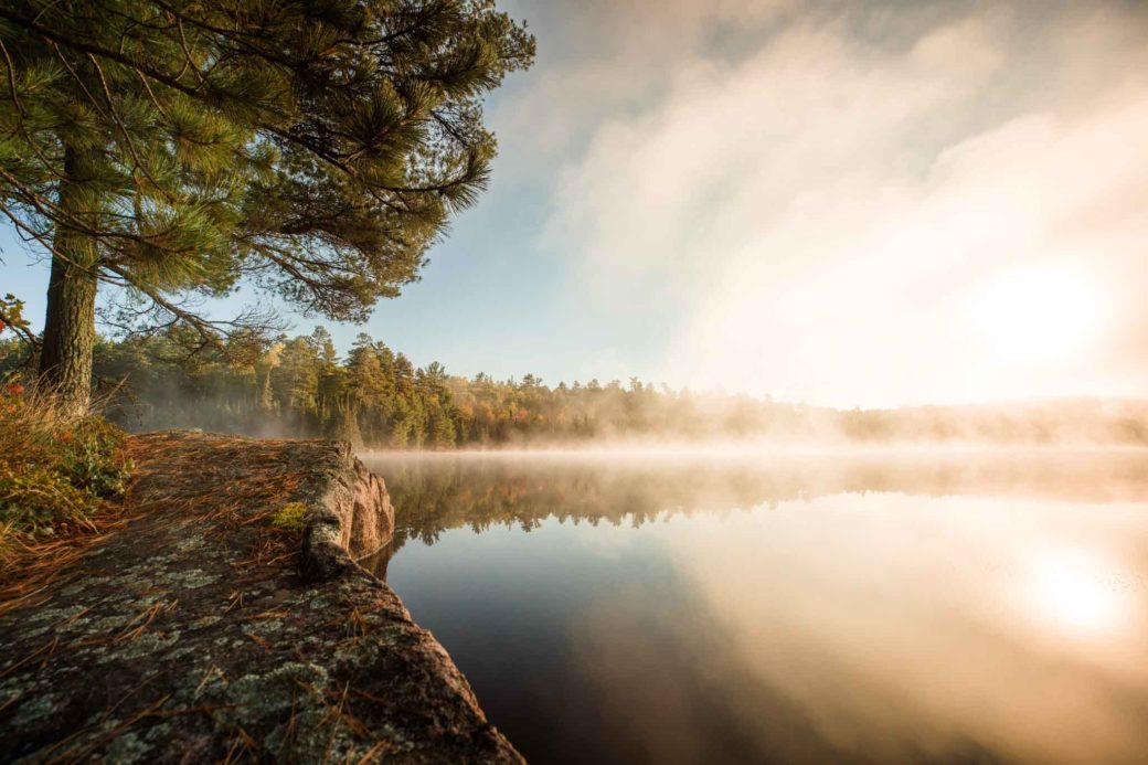 Landscape editorial photo of Boundary Waters Canoe Area with fog over the water at sunrise.